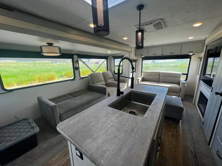 Spacious RV rental interior featuring a sleek kitchen island, comfortable sofas, and panoramic windows with scenic field views.. Forest River Vibe 2022