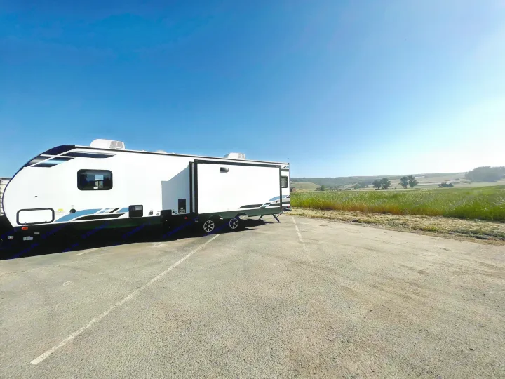 White RV rental parked in a sunny lot, overlooking rolling green hills and fields under a clear blue sky.. Forest River Vibe 2022