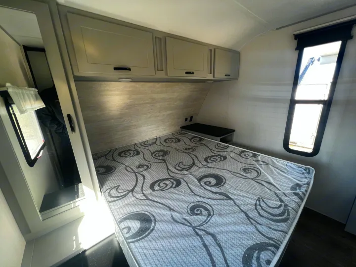 Inside a modern RV rental bedroom, featuring a patterned mattress, overhead cabinets, and natural light from windows.. Forest River Vibe 2022