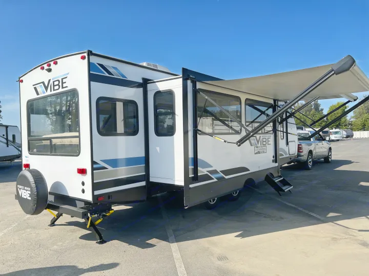 This white Forest River Vibe travel trailer, ideal for an RV rental, features an extended slide-out, awning, and rear tire cover.. Forest River Vibe 2022