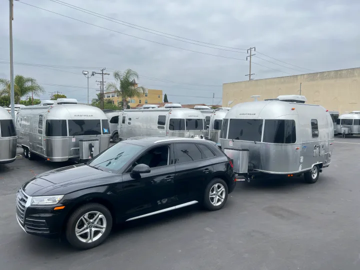 Black Audi SUV towing a shining Airstream RV rental, one of many travel trailers on a cloudy day.. Airstream Bambi 2023