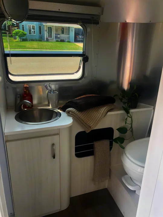 This clean RV rental bathroom features a compact sink, toilet, and thoughtful touches like folded towels and a small plant, maximizing space.. Airstream Sport 2019