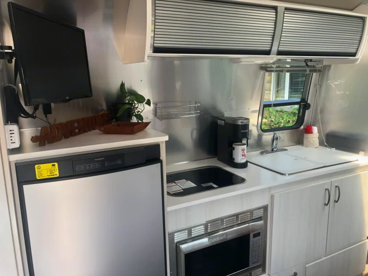 RV rental interior: compact kitchen area featuring a Dometic refrigerator, Cuisinart microwave, sink, Keurig coffee maker, and mounted TV.. Airstream Sport 2019