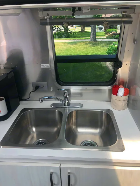 RV rental kitchen: stainless steel double sink, modern faucet, coffee maker, and window view of a green landscape.. Airstream Sport 2019