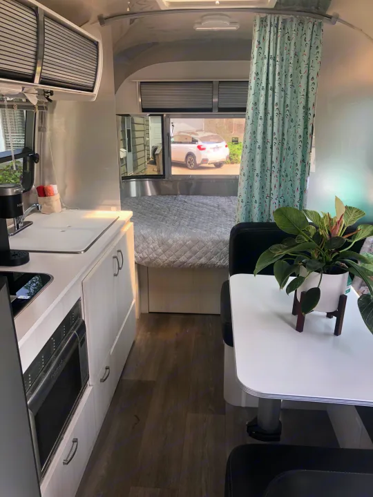 Modern RV rental interior showcasing a compact kitchen, comfortable bed, and dining space with a yoga-patterned curtain.. Airstream Sport 2019