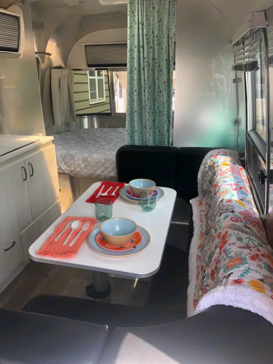 A stylish rv rental interior showing a dining table set for two, a comfortable bed, and a compact kitchen.. Airstream Sport 2019