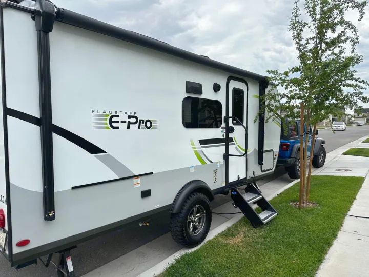 Experience camping with this white Flagstaff E-Pro rv rental, a travel trailer parked beside a blue Jeep on a residential street.. Forest River Flagstaff E-Pro 2023