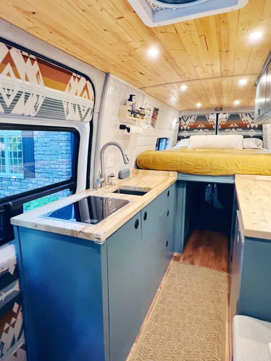 Cozy RV rental interior: Features a modern kitchen with teal cabinets, wood counters, a raised bed, and a wooden ceiling.. Freightliner Sprinter 2500 2019
