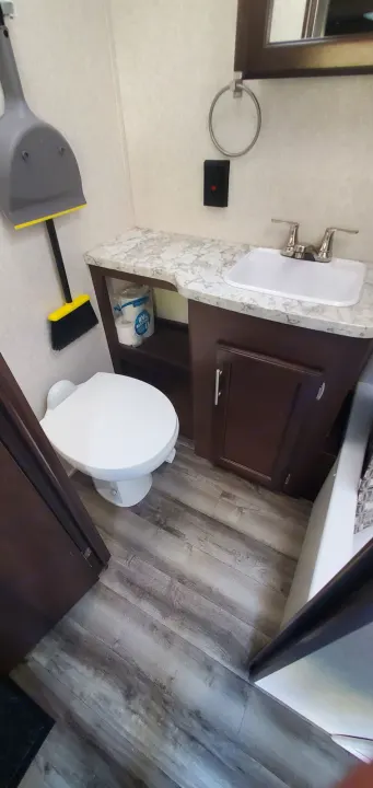RV rental bathroom interior: compact, with toilet, sink, vanity storage, and wood-look floor. Broom & dustpan on wall.. Jayco Flight 2020