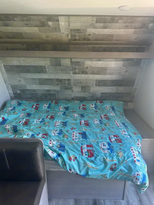 Cozy RV rental bed features a fun camper-themed comforter and rustic wood-paneled walls, perfect for travelers.. Dutchmen Coleman Lantern LT 2022