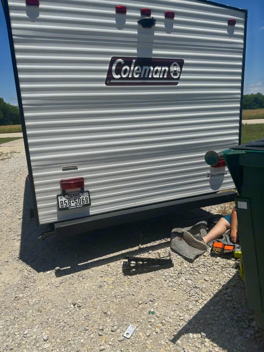 RV rental: Rear of a Coleman travel trailer with a Texas plate, person working underneath.. Dutchmen Coleman Lantern LT 2022