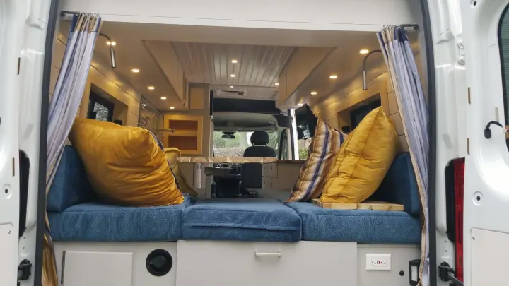 Step inside this inviting RV rental! A comfy camper van interior featuring blue seating, accent pillows, and warm ambient lighting.. Ram 3500 Extended 2021