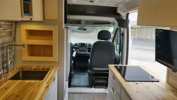 Inside a modern RV rental: view from the kitchen with wood counters, sink, and cooktop, looking towards the driver's cab.. Ram 3500 Extended 2021