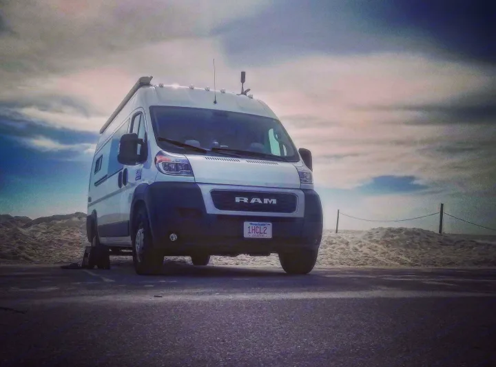 White Ram ProMaster camper van, an excellent rv rental choice, parked by sandy dunes under a cloudy sky.. Ram 3500 Extended 2021