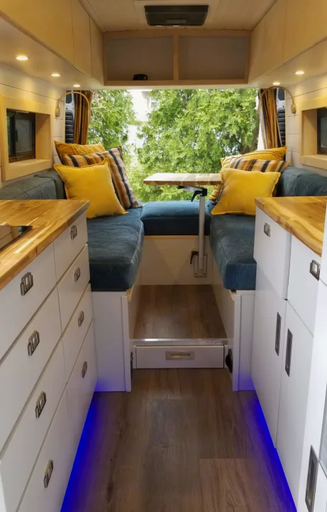 RV rental's inviting interior: bright kitchenette, dining area with comfy blue cushions, and a lush green outdoor view.. Ram 3500 Extended 2021