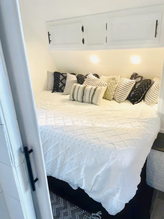 Modern rv rental bedroom interior featuring a cozy white bed with stylish black and white patterned pillows.. Forest River Cherokee Grey Wolf 2019