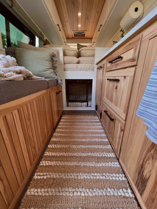 Cozy RV rental interior featuring custom wood cabinetry, a built-in dog crate, comfortable seating, and a stylish rug.. Mercedes-Benz Sprinter 2021