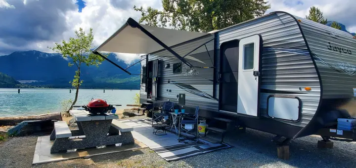 Relaxing at a scenic lakeside RV rental campsite, featuring an extended awning, BBQ, and mountain views.. Jayco Jay Flight SLX Rocky Mountain Edition 2021
