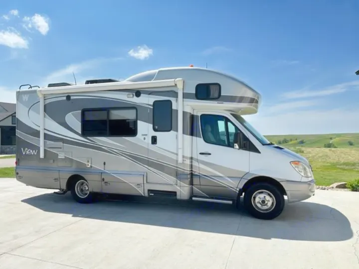 A sleek gray and white Winnebago View RV rental parked on a sunny paved driveway with grassy hills.. Winnebago View 2011