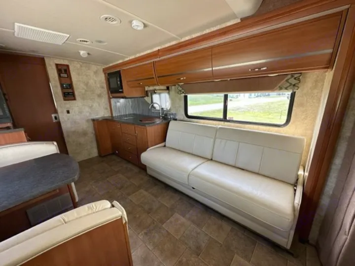 Spacious RV rental interior: beige sofa, wood kitchen, dining table, tiled floor, and bright windows.. Winnebago View 2011
