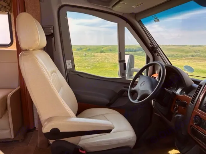 Inside an RV rental: a plush cream driver's seat, Mercedes dashboard, and a wide view of rolling green hills. Ready for adventure!. Winnebago View 2011