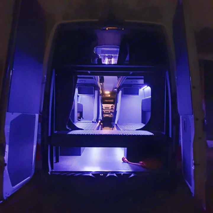 Cozy blue-lit RV rental interior from open rear doors, showing bunk beds & a front sleeping platform.. Mercedes Sprinter Freight Liner 2020