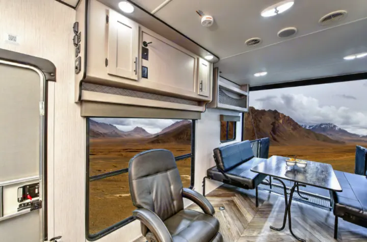 Inside a bright RV rental: a leather recliner, dinette, and modern cabinets, all looking out to vast mountains and desert.. Heartland Lithium 2515S 2022
