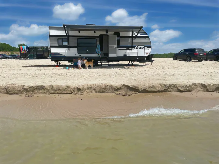 An RV rental provides beachfront camping: a family with a child and dog relax by the steps on the sandy shore with water in the foreground.. Heartland Lithium 2515S 2022