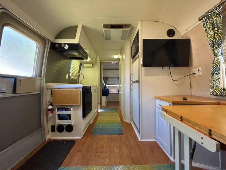 Inside an RV rental: a compact yet complete kitchen, living area with TV, and hallway leading to the rear sleeping space.. Airstream Excella 2000