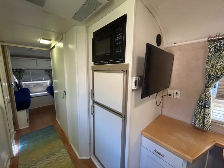 Clean and compact RV rental interior showing kitchen with microwave, fridge, TV, and rear living space.. Airstream Excella 2000