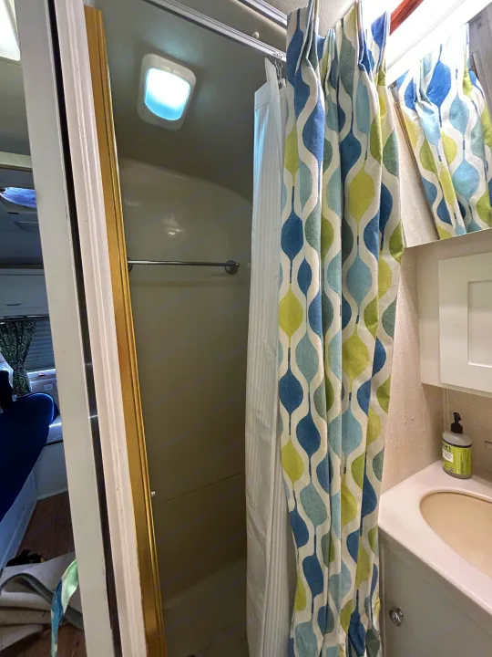 Bright RV rental bathroom with a compact shower stall, vibrant patterned curtain, and sink vanity.. Airstream Excella 2000