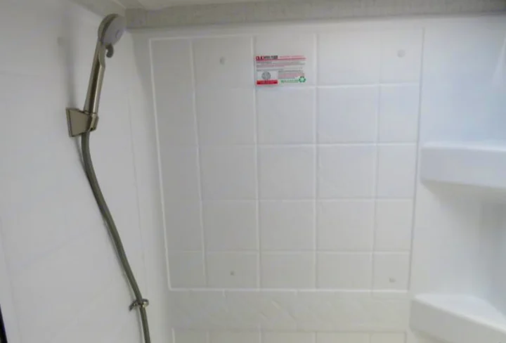 Compact RV rental shower with white tiled walls, hand-held shower, and corner shelving.. Winnebago Micro Minnie FLX 2100BH 2022