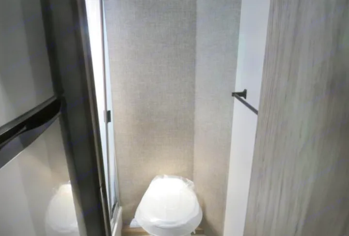 This RV rental's compact bathroom features a new, plastic-covered toilet, a towel bar, and textured walls.. Winnebago Micro Minnie FLX 2100BH 2022