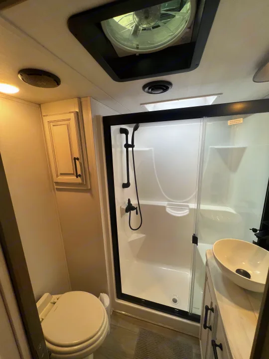 Step inside this modern RV rental bathroom featuring a black-framed shower, toilet, and stylish vessel sink.. Keystone RV Montana Legacy Edition 2022
