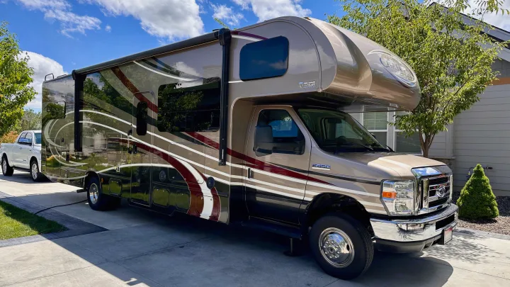 A large, tan and brown Class C RV, ideal for rv rental travel, is parked on a sunny driveway, ready for your next adventure.. Thor Chateau 2018