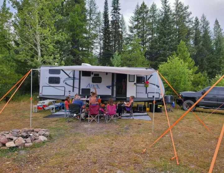 Relaxing family camping trip with an RV rental. People enjoy the outdoors under an awning beside a fire pit.. Coachmen Apex 2015