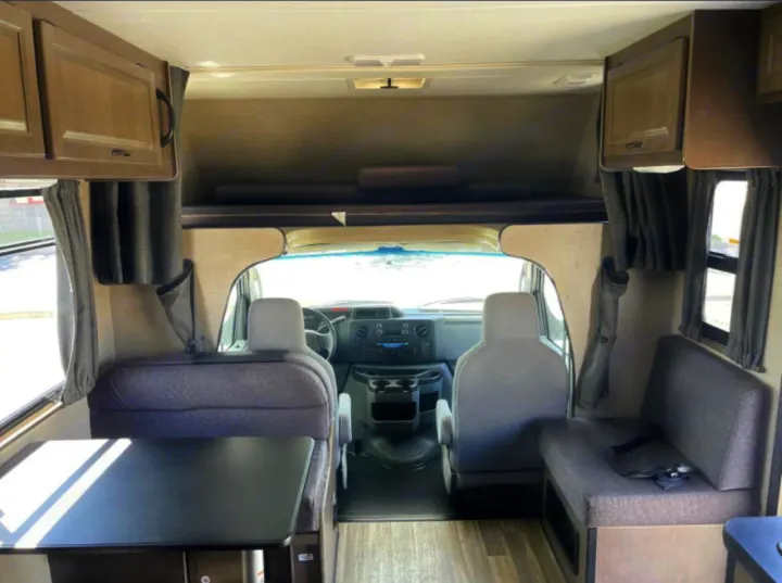 RV rental interior: driver's cabin, over-cab bunk, and dinette with seating on both sides visible from the rear.. Thor Majestic 2018