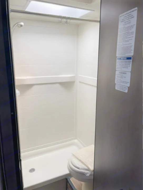 RV rental's compact bathroom: a clean, well-lit white shower stall with overhead skylight, and a toilet.. Thor Majestic 2018