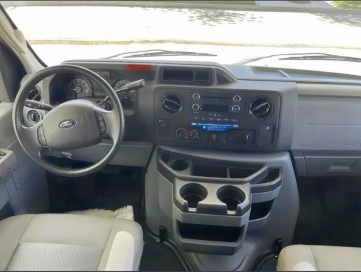 RV rental Ford van interior: Driver's view of the dashboard, steering wheel, and center console with cup holders.. Thor Majestic 2018