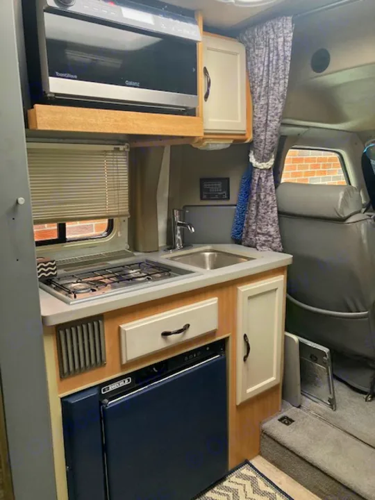 Inside an RV rental: a compact kitchen featuring a microwave, sink, and two-burner stove. Essential amenities for your travels.. Winnebago Rialta 1998