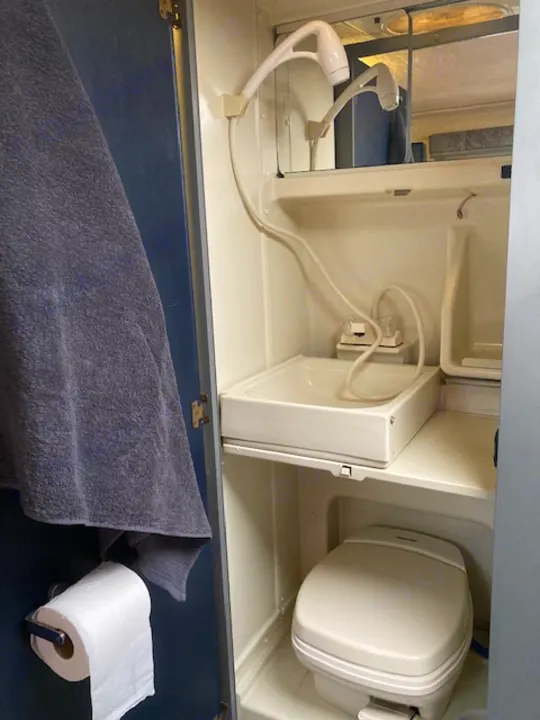 This RV rental displays its compact bathroom with handheld showers, a folding toilet, and fold-down counter. Towel & TP ready.. Winnebago Rialta 1998