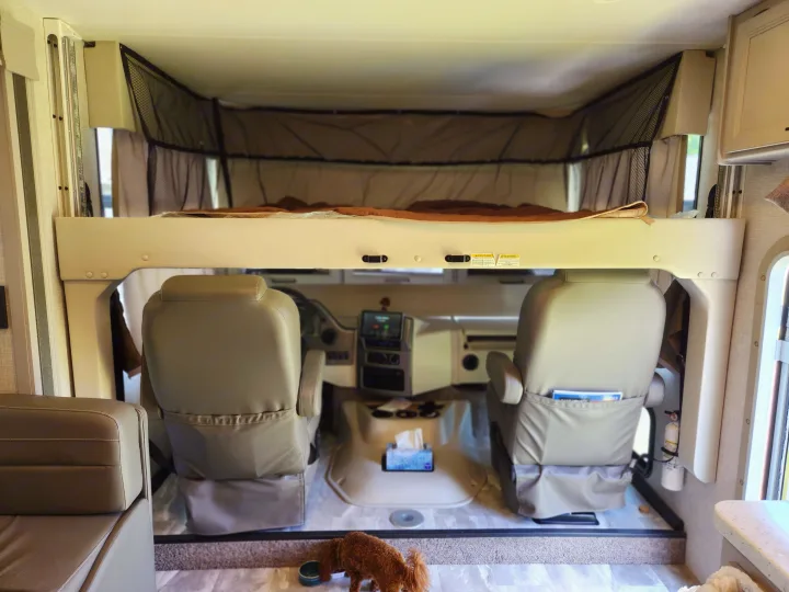 Inside an RV rental, showing the front cabin with driver/passenger seats, an overhead bunk, and a dog on the floor.. Thor Windsport 2023