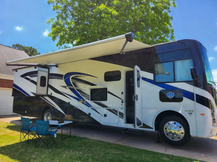 A modern RV rental parked on a sunny day. Features extended awning, slide-out, and outdoor TV. Perfect for travel.. Thor Windsport 2023