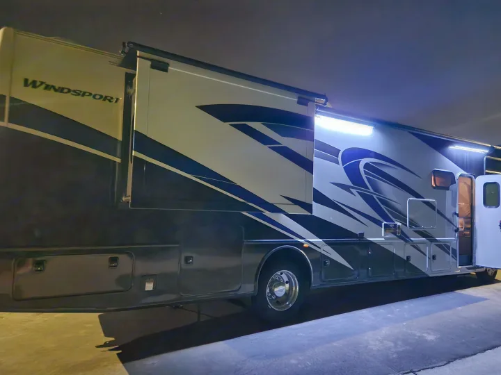 RV rental: Brightly lit Thor Windsport motorhome with extended slide-outs and awning, parked at night.. Thor Windsport 2023
