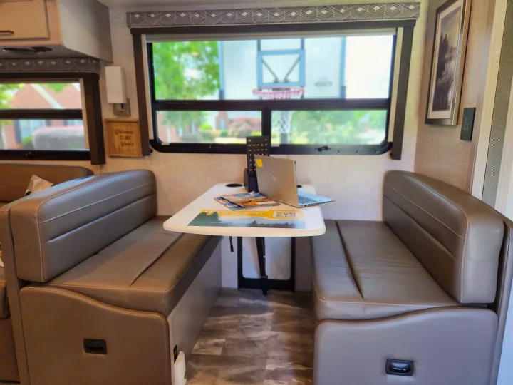 This RV rental features a cozy dinette workspace, complete with a table, laptop, comfy benches, and a large window view.. Thor Windsport 2023