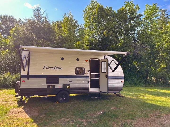 Relax in this Friendship travel trailer RV rental, set up outdoors with its awning extended and door open on a sunny day.. Gulf Stream Friendship 2022