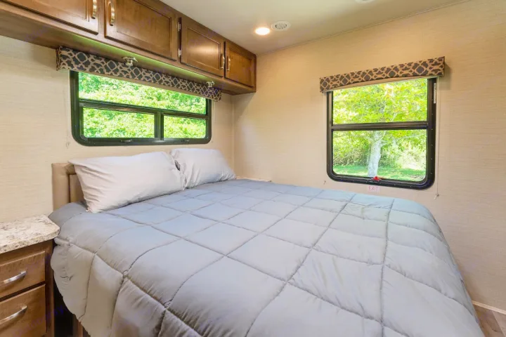 This **rv rental** bedroom features a cozy bed, nature views from windows, and overhead storage cabinets.. Jayco Redhawk 2019