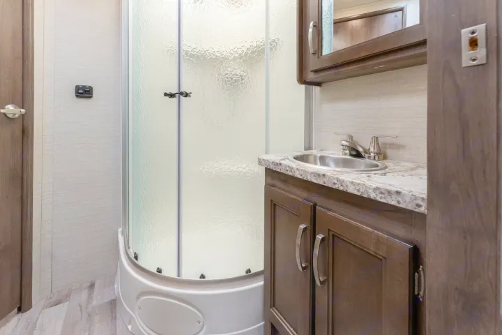 RV rental bathroom featuring a compact corner shower with frosted glass doors, a vanity with sink, and a mirrored cabinet.. Jayco Redhawk 2019
