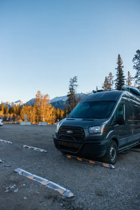 A dark gray Ford Transit campervan in a scenic mountain lot with fall trees, ready for your RV rental adventure.. Ford Transit Custom 2019