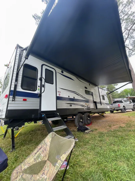 Travel trailer RV rental parked with awning extended, showing entry steps, a camping chair, and a truck nearby.. Keystone RV Springdale 2023